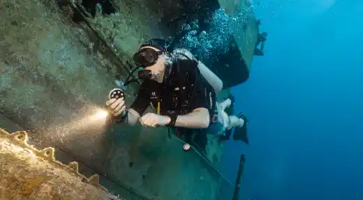Scuba diver using a torch while exploring the exterior of a shipwreck during advanced wreck training in Koh Tao, Thailand