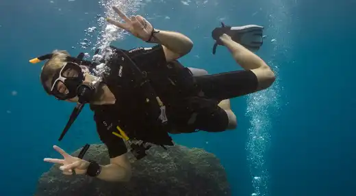 Scuba diver giving a peace sign while diving over a coral reef in Koh Tao, Thailand
