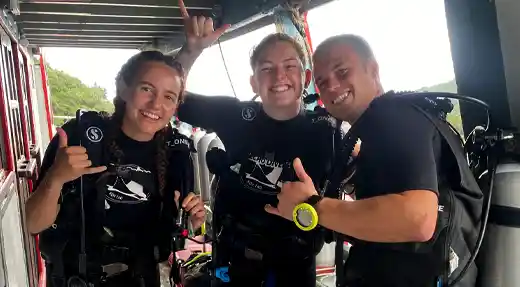 Three smiling divers on the Echo Divers Koh Tao boat showing shaka signs before their dive.