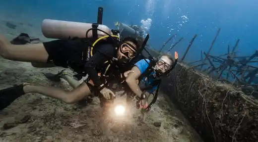  Two divers exploring a shallow wreck while being filmed with an underwater video light during a Liquid Light Studio session with Echo Divers Koh Tao. 